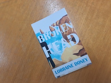 A copy of Lorraine's book, Broken Head, with the front cover showing an illustration of the Broken Head cliff face.