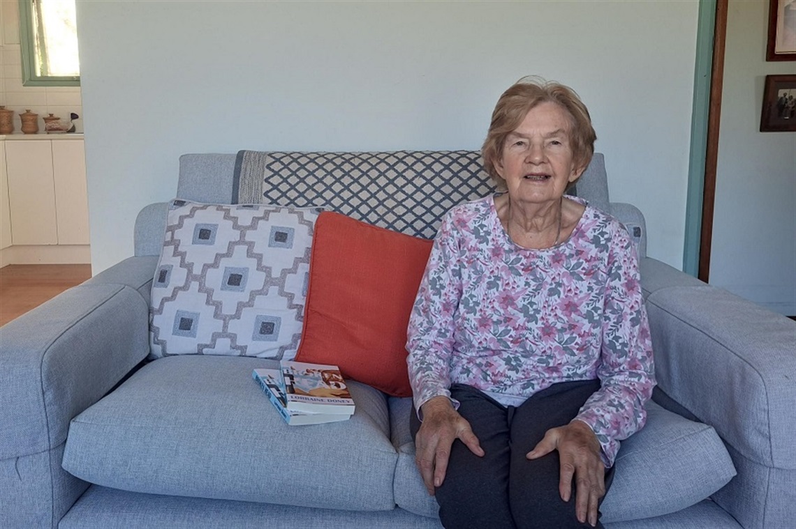 Lorraine sits on her couch with copies of her novel, Broken Head, next to her.