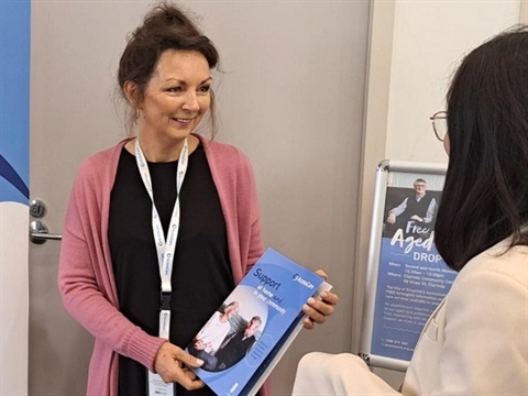 AccessCare team member holds a brochure while she is talking to a lady. 
