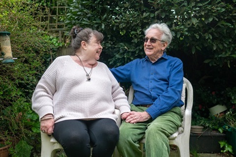 An elderly couple laugh together in their backyard