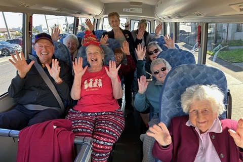 AccessCare's community bus clients cheer while sitting on the bus, ready to head off on an adventure.