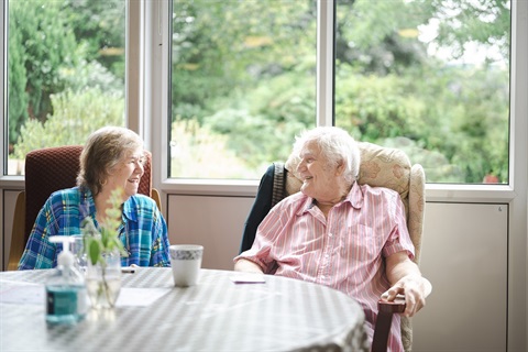 An older couple sit at their dining table together.