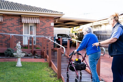 An AccessCare support worker assists a client with a walker up the ramp to her front door. 