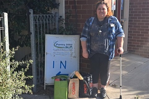 Client Julie stands beside a sign for the Pantry 5000 food bank.