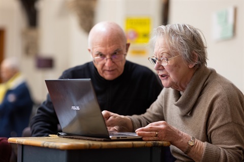 Two elderly people use a laptop computer together. 