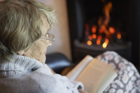 an elderly person with a warm blanket and book in front of a fire