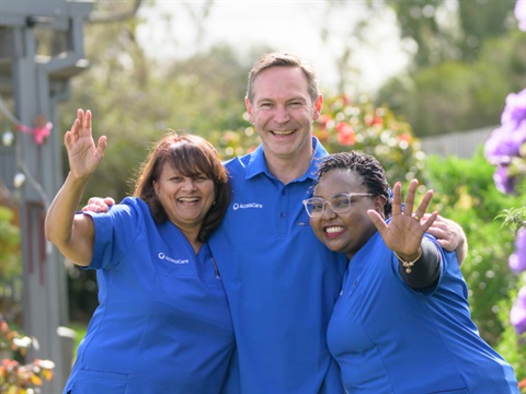 a group of three tesam members from AccessCare stand in a garden. They are wearing blue shirts.