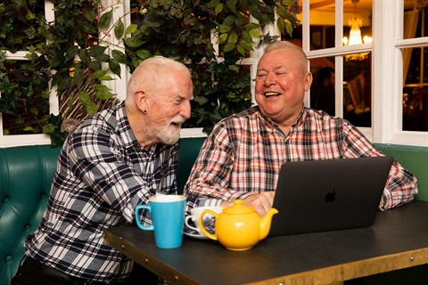 Two men sit together at a laptop.